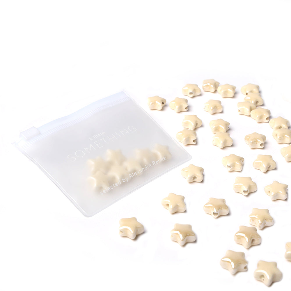 Alexandra Renke kleine, beigefarbene Bonbons in Sternform, die aus einem durchsichtigen, wiederverschließbaren Beutel auf eine weiße Oberfläche tropfen - ideal, um sie selbst zu machen und Ihren Kreationen einen skurrilen Touch zu verleihen.