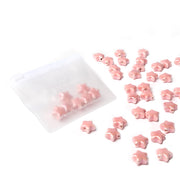 Ein durchsichtiges Etui von Alexandra Renke mit kleinen rosafarbenen, sternförmigen, glasierten Keramikperlen, von denen einige im Inneren und andere in der Nähe verstreut sind - perfekt, um einzigartigen Schmuck zu kreieren.