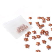 Kleine, glänzende Sternform-Perlen von Alexandra Renke, verstreut in einem durchsichtigen Reißverschlussbeutel auf weißem Hintergrund - perfekt, um Ihren eigenen Schmuck mit himmlischem Charme zu gestalten.