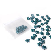 Die teal Sternform glasierten Keramikperlen von Alexandra Renke sind auf weißem Hintergrund neben einem halbtransparenten Beutel verstreut - ideal zur kreativen Schmuckgestaltung.