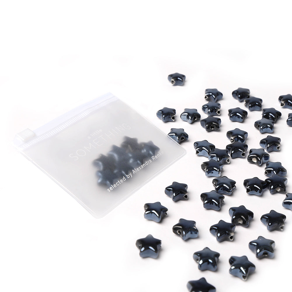 Ein durchsichtiger Beutel mit schwarzen Sternform Perlen von Alexandra Renke, mit zusätzlichen Perlen auf weißem Hintergrund - ideal für die Schmuckherstellung.