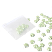 Hellgrüne, sternförmige Keramikperlen von Alexandra Renke ergießen sich aus einem durchsichtigen Reißverschlussbeutel auf eine weiße Oberfläche - perfekt für die Herstellung von DIY-Schmuck.