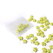 Kleine grüne, sternförmige, glasierte Keramikperlen von Alexandra Renke quellen aus einem durchsichtigen Beutel auf weißem Grund - ideal für die Schmuckherstellung.