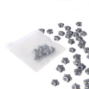 Eine gefrostete Reißverschlusstasche von Alexandra Renke mit glasierten Keramiksternperlen für die Schmuckherstellung ergießt sich auf eine weiße Oberfläche.