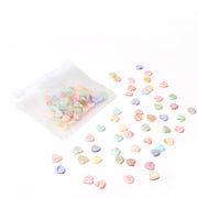 Kleine pastellfarbene Herzperlen von Alexandra Renke, darunter Muschelperlen Herzform, befinden sich neben einem durchsichtigen Reißverschlussbeutel auf weißem Grund - ideal zum Schmuck basteln oder als Ergänzung zu Ihrem Lieblings-Perlen-Mix.