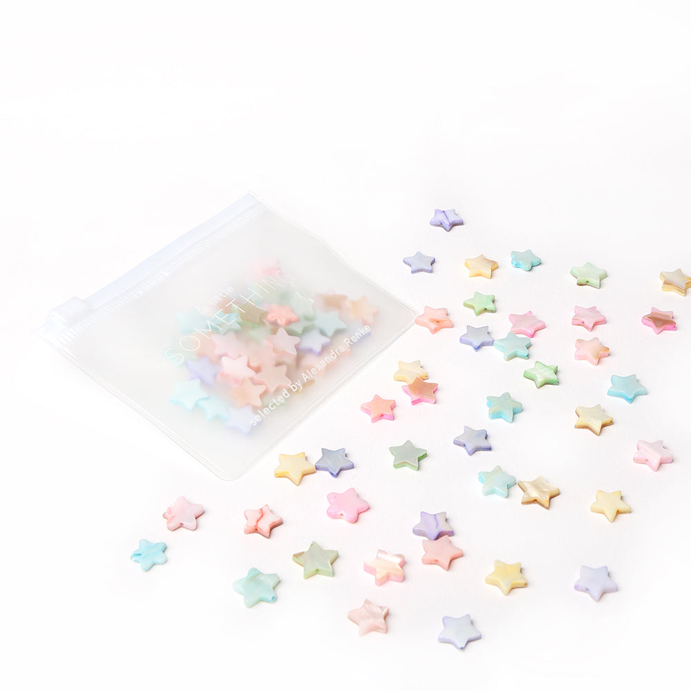 Ein durchsichtiges Etui von Alexandra Renke fasst pastellfarbene Radiergummis in Sternform auf weißer Oberfläche - perfekt, um Schmuck selbst zu machen oder Ihren kreativen Projekten Sternform-Charme zu verleihen.