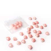 Kleine rosa glasierte Keramikperlen von Alexandra Renke verstreut neben einem gefrosteten Reißverschlussbeutel auf weißem Hintergrund - ideal für Schmuck basteln und kreative Schmuckdesigns.