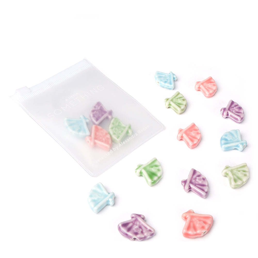 Bunte, fächerförmige Keramikperlen in Fächerform von Alexandra Renke verstreut neben einer halbtransparenten Reißverschlusstasche auf Weiß - perfekt für Schmuck selber machen Projekte.