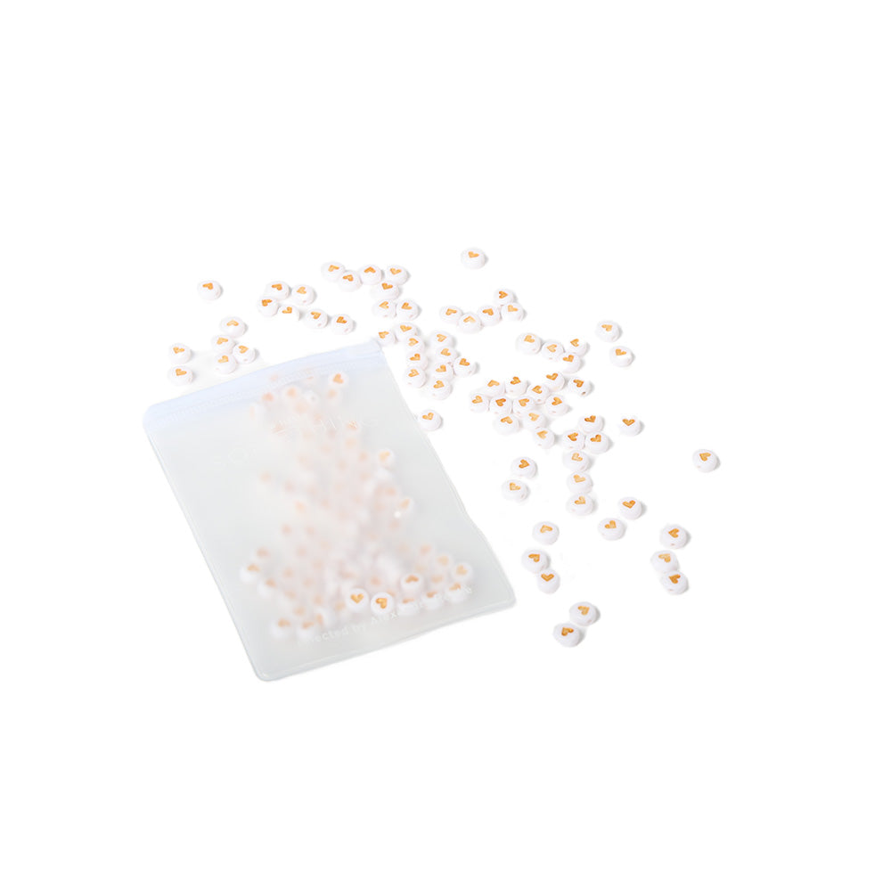 Ein kleines Plastiksäckchen mit winzigen Herzchen Perlen und runden Perlen von ☆, ideal für Schmuck basteln, auf weißem Hintergrund.