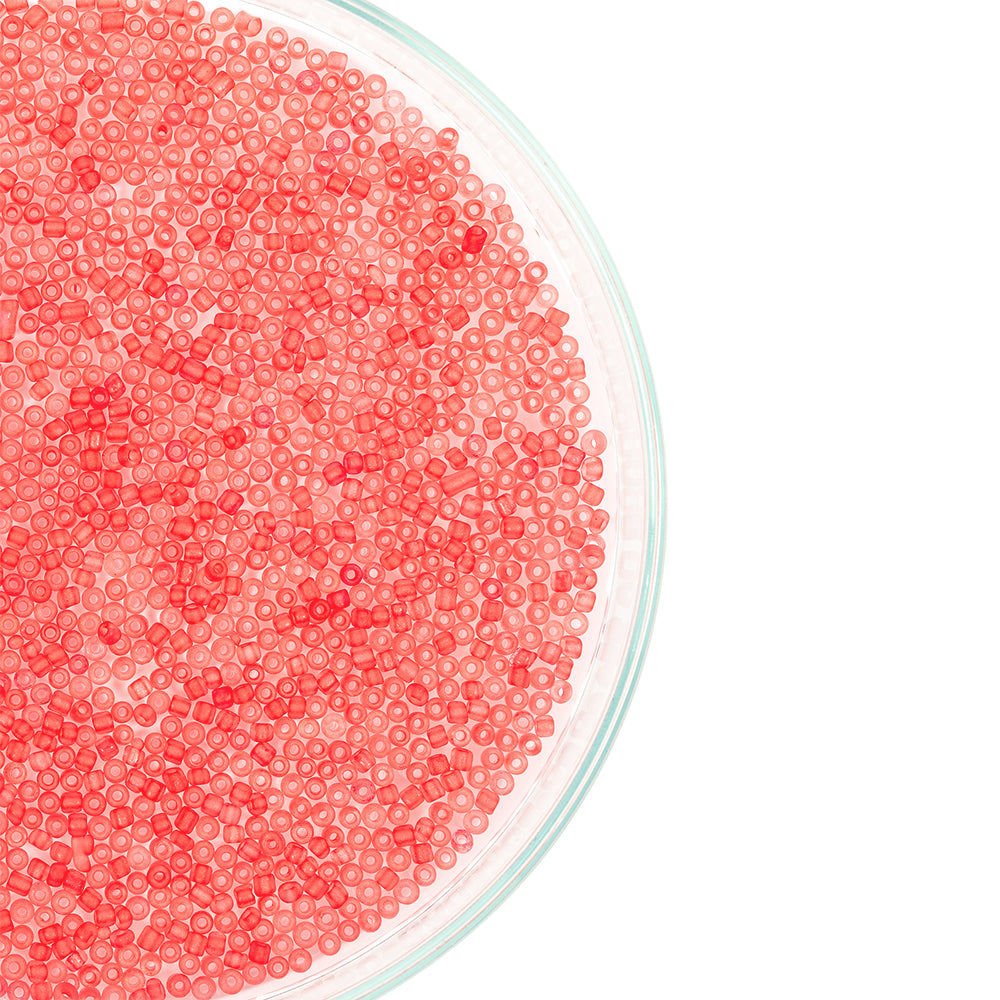 Eine Glasschale, gefüllt mit vielen kleinen, runden, durchscheinend rosa Mini-Glasperlen vor weißem Hintergrund – ideal zum Schmuckbasteln oder für kreative Projekte mit Bastelperlen.