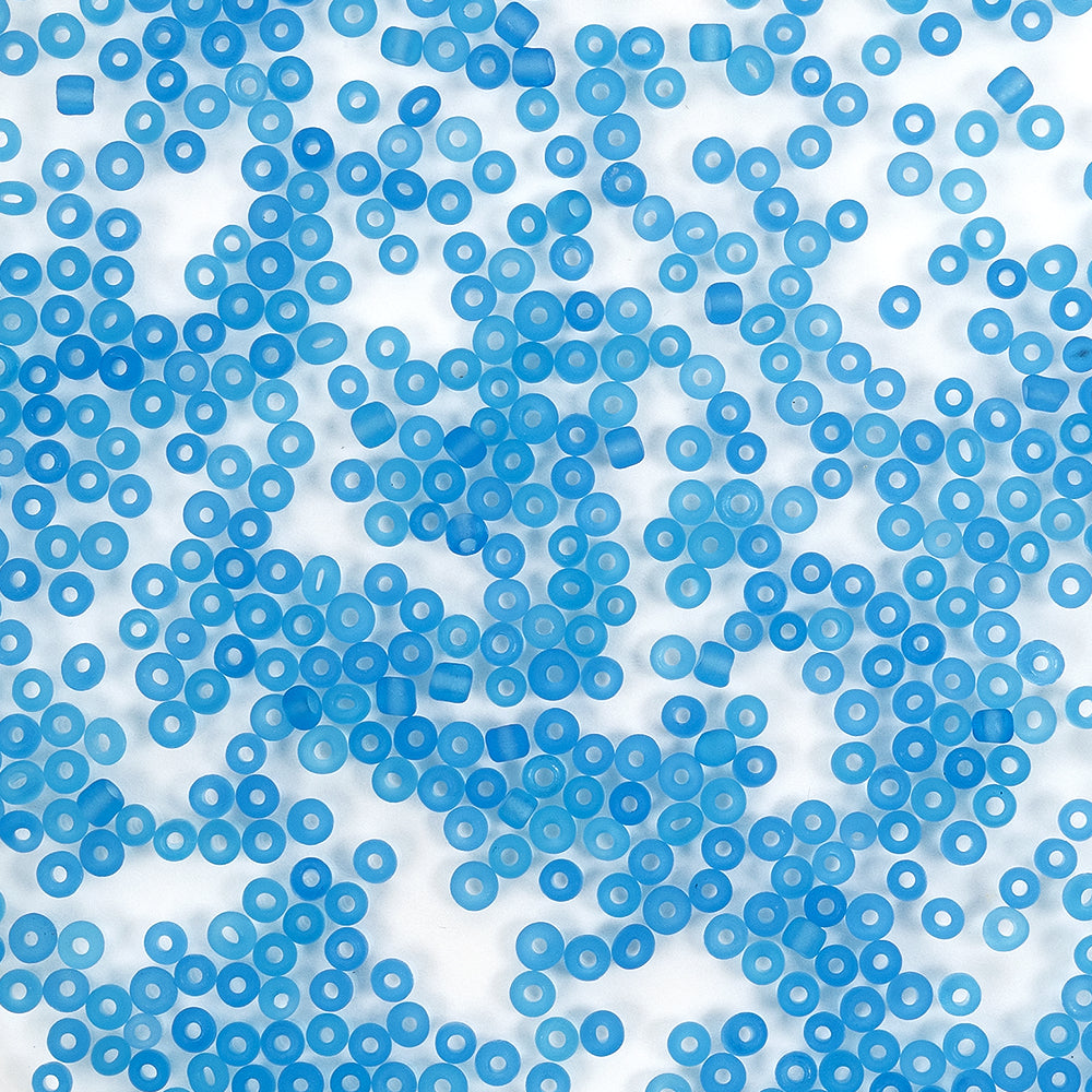 Auf einem weißen Hintergrund sind von oben betrachtet viele kleine, blaue, durchscheinende Mini-Glasperlen verstreut – ideal für Bastelprojekte oder alle, die Schmuck basteln möchten.
