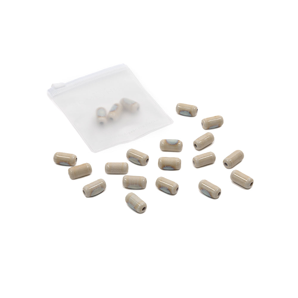 Kleine, beige glasierte Keramikperlen, verstreut neben einem durchscheinenden Säckchen auf weißem Hintergrund – perfekte Perlen zum Auffädeln, um selbst Schmuck herzustellen.