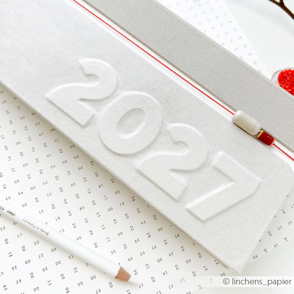 Weißes Federmäppchen mit der Prägung „2027“, das auf einem gepunkteten Blatt Papier liegt, darauf ein Bleistift und ein Radiergummi – ideal zum Ordnen deiner Utensilien für das Perlenbasteln oder die Schmuckherstellung, wie zum Beispiel glasierte Keramikperlen.