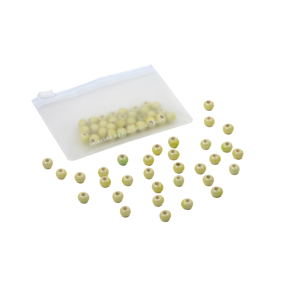 Kleine, runde, grüne, handgefertigte Perlen, verstreut neben einem durchsichtigen Beutel, in dem sich weitere glasierte Keramikperlen befinden, auf weißem Hintergrund – perfekt für alle, die selbst Schmuck herstellen möchten.