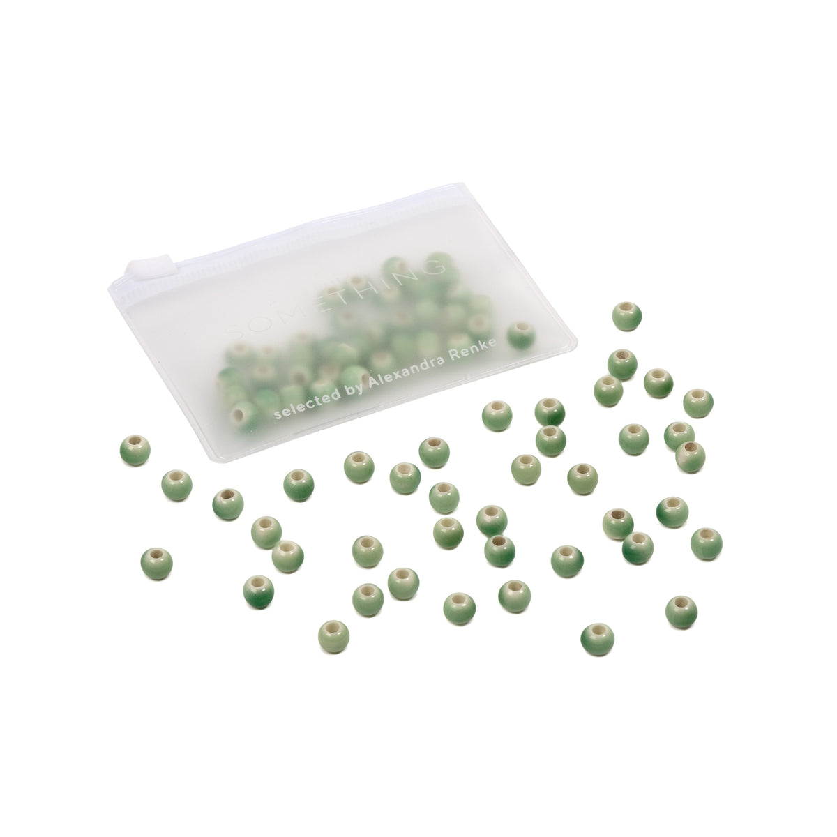 Kleine grüne Perlen liegen verstreut neben einem durchsichtigen Beutel mit Reißverschluss, der weitere handgefertigte Perlen enthält – perfekt für alle, die selbst Schmuck herstellen möchten und eine Vorliebe für glasierte Keramikperlen haben.
