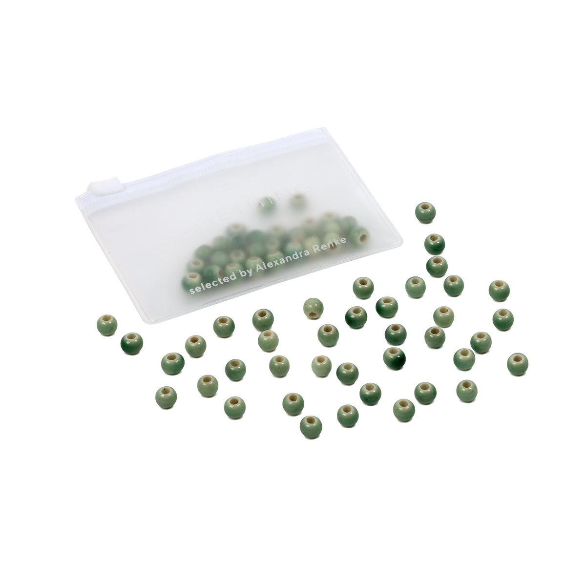 Kleine grüne Perlen, darunter auch handgefertigte Perlen, liegen verstreut neben einem durchsichtigen Reißverschlussbeutel, in dem sich einige Perlen befinden – perfekt für alle, die selbst Schmuck basteln möchten.