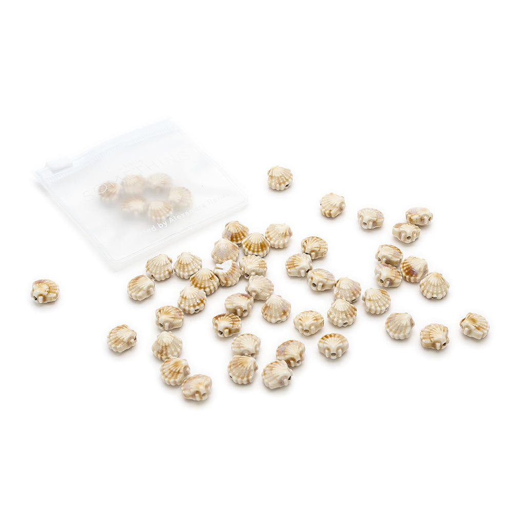 Kleine, goldgerippte Perlen von Alexandra Renke sind auf einer weißen Fläche verstreut, einige davon in einem durchsichtigen Plastikbeutel, wodurch der Charme handgefertigter Perlen zur Geltung kommt.