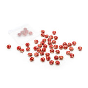 Auf einem weißen Hintergrund liegen verstreut rote Glasperlen von Alexandra Renke mit goldenen Akzenten sowie handgefertigte Perlen in Muscheloptik neben einem kleinen durchsichtigen Plastikbeutel.
