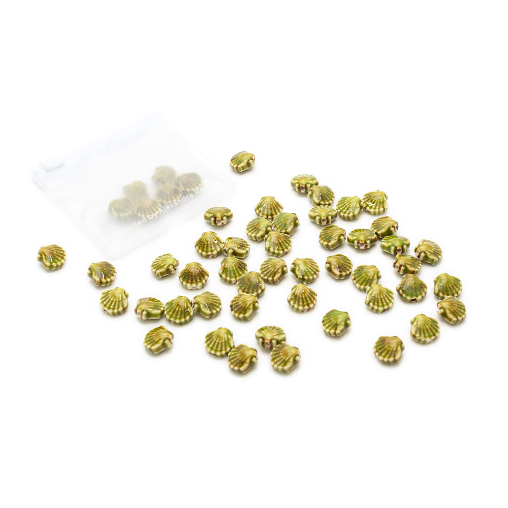 Kleine handgefertigte Perlen in Gold und Grün im Muschel-Look von Alexandra Renke liegen neben einer durchsichtigen Plastiktüte, in der sich weitere Perlen befinden.