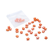 Kleine orange glasierte Keramikperlen im Seestern-Design von Alexandra Renke sind auf weißem Hintergrund in der Nähe eines durchsichtigen Plastikbeutels verstreut.