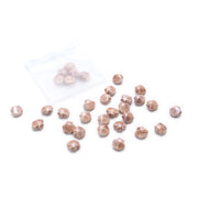 Kleine, braune, muschelförmige Keramikperlen von Alexandra Renke in Muscheloptik liegen verstreut neben einem durchsichtigen Beutel auf weißem Hintergrund.