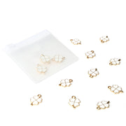 Alexandra Renke Gold und Weiß Glücksklee Charm Schmuckanhänger verstreut an einem durchsichtigen Beutel auf Weiß, ideal als Buchbinde Zubehör oder zur Schmuckherstellung.