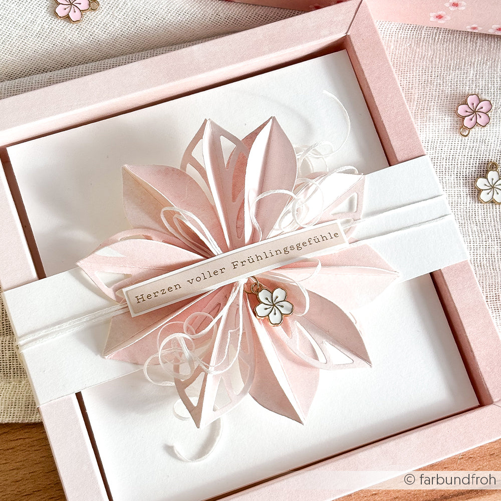 Eine handgemachte rosa-weiße Karte von Alexandra Renke mit einer 3D-Papierblume, Kirschblüten-Charm und einem Etikett "Herzen voller Frühlingsgefühle" - perfekt für Papierprojekte oder als Inspiration für Buchbindearbeiten.
