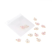 Die kleinen rosafarbenen und weißen Kirschblüten-Charm-Anhänger mit Goldrand von Alexandra Renke sitzen neben einem durchscheinenden weißen Reißverschlussbeutel - ideales Buchbindezubehör für Papierprojekte-Anhänger.