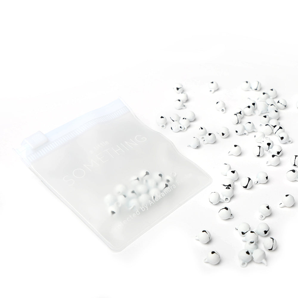 Ein durchsichtiges Täschchen mit kleinen weißen Perlen von Alexandra Renke, ideal für Bastelkreationen oder Scrapbooking, mit ein paar verstreuten Perlen auf weißem Hintergrund.