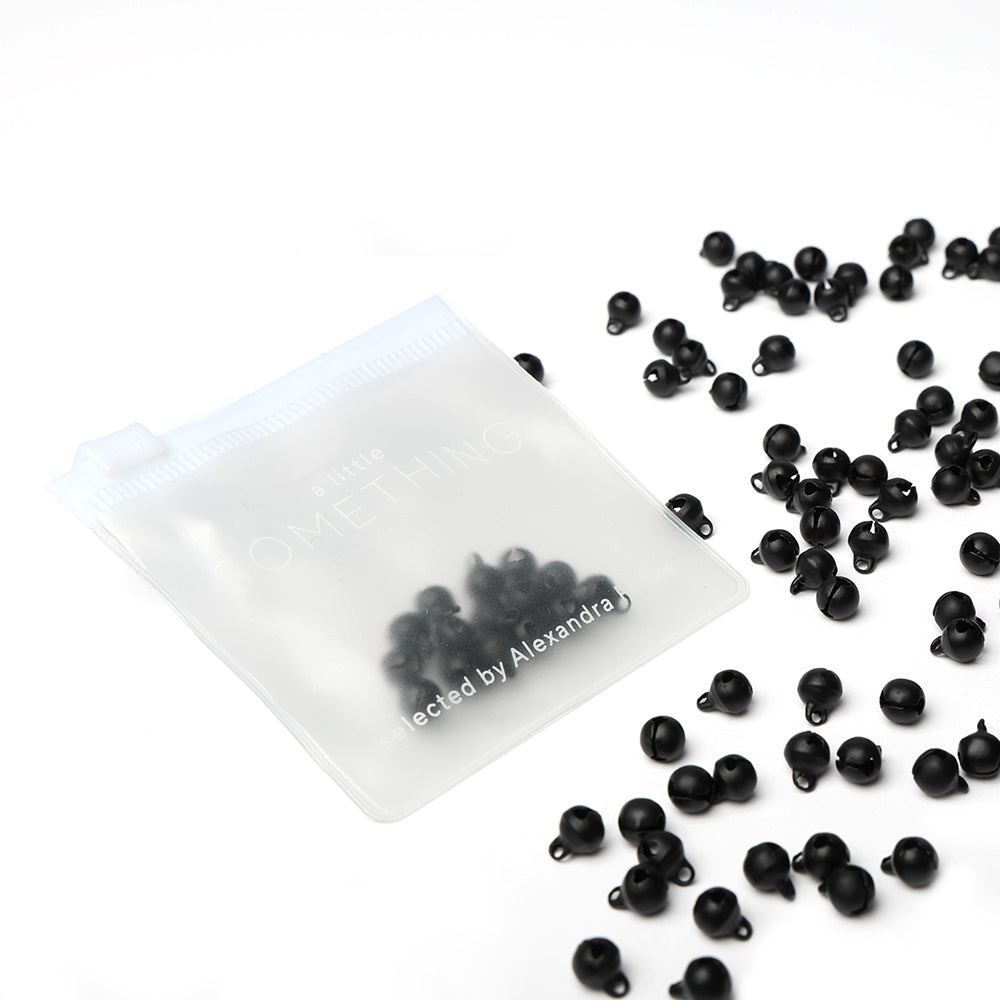 Ein gefrostetes Reißverschlusstäschchen von Alexandra Renke, gefüllt mit schwarzen Perlen - ideal zum Basteln oder Scrapbooking - umgeben von vielen losen schwarzen Perlen.