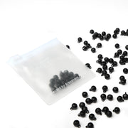 Ein gefrostetes Reißverschlusstäschchen von Alexandra Renke, gefüllt mit schwarzen Perlen - ideal zum Basteln oder Scrapbooking - umgeben von vielen losen schwarzen Perlen.