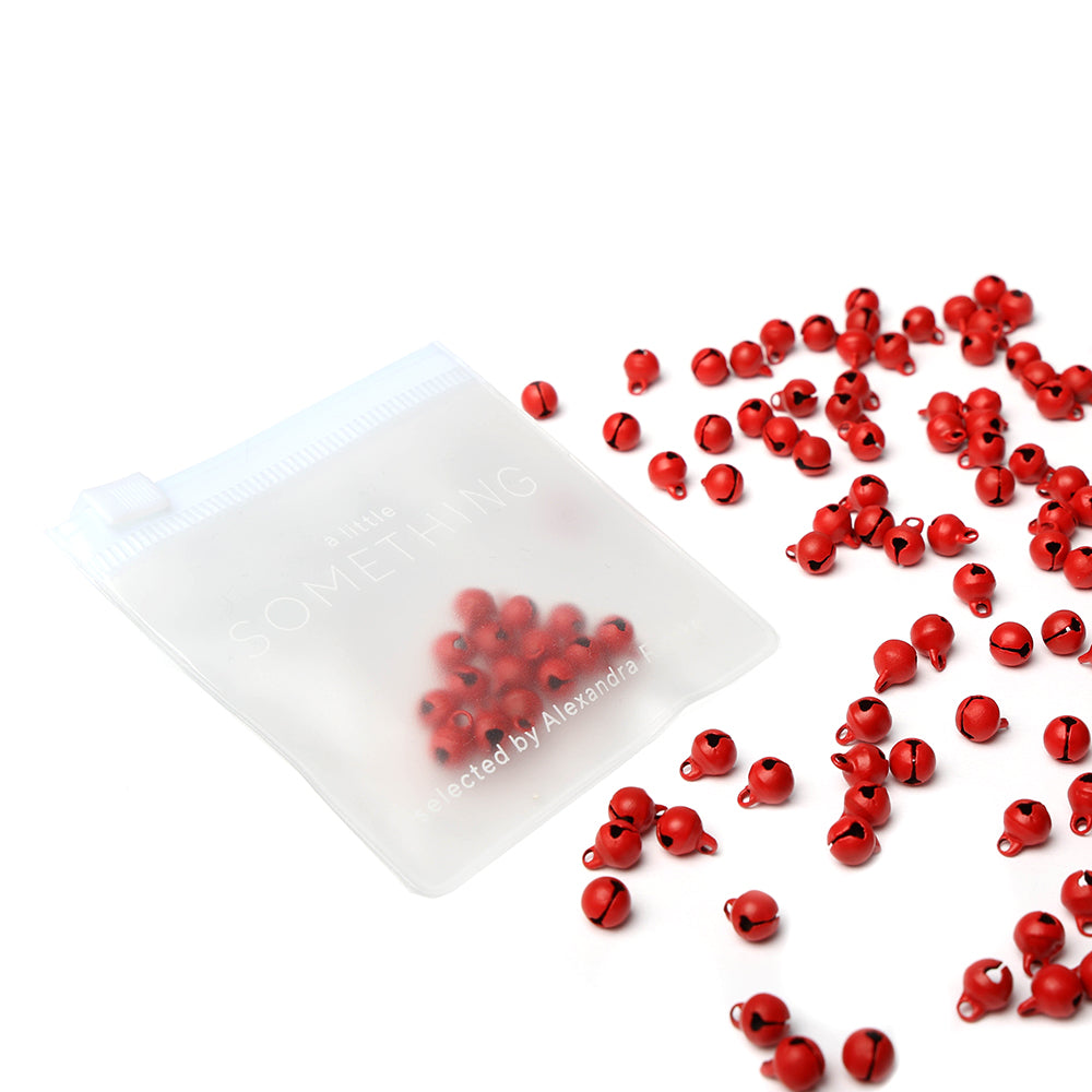 Kleine rote Perlen von Alexandra Renke verstreut neben einem durchsichtigen Beutel, mit einigen Perlen darin - ideal für Bastelkreationen oder Scrapbooking-Projekte.