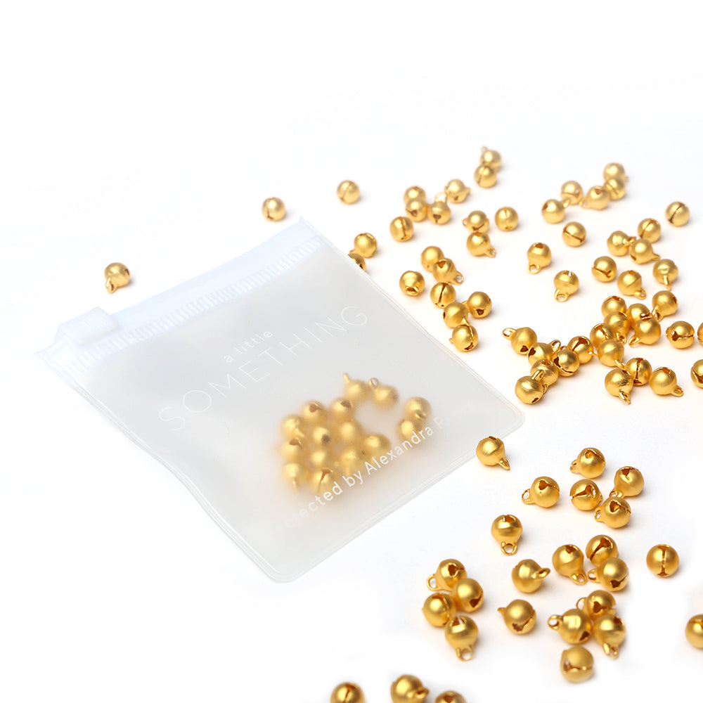 Ein gefrosteter Beutel gefüllt mit goldenen Perlen und mehr auf einer weißen Oberfläche - ideal für Bastelkreationen oder um Ihrem Scrapbooking Glanz zu verleihen, von Alexandra Renke.