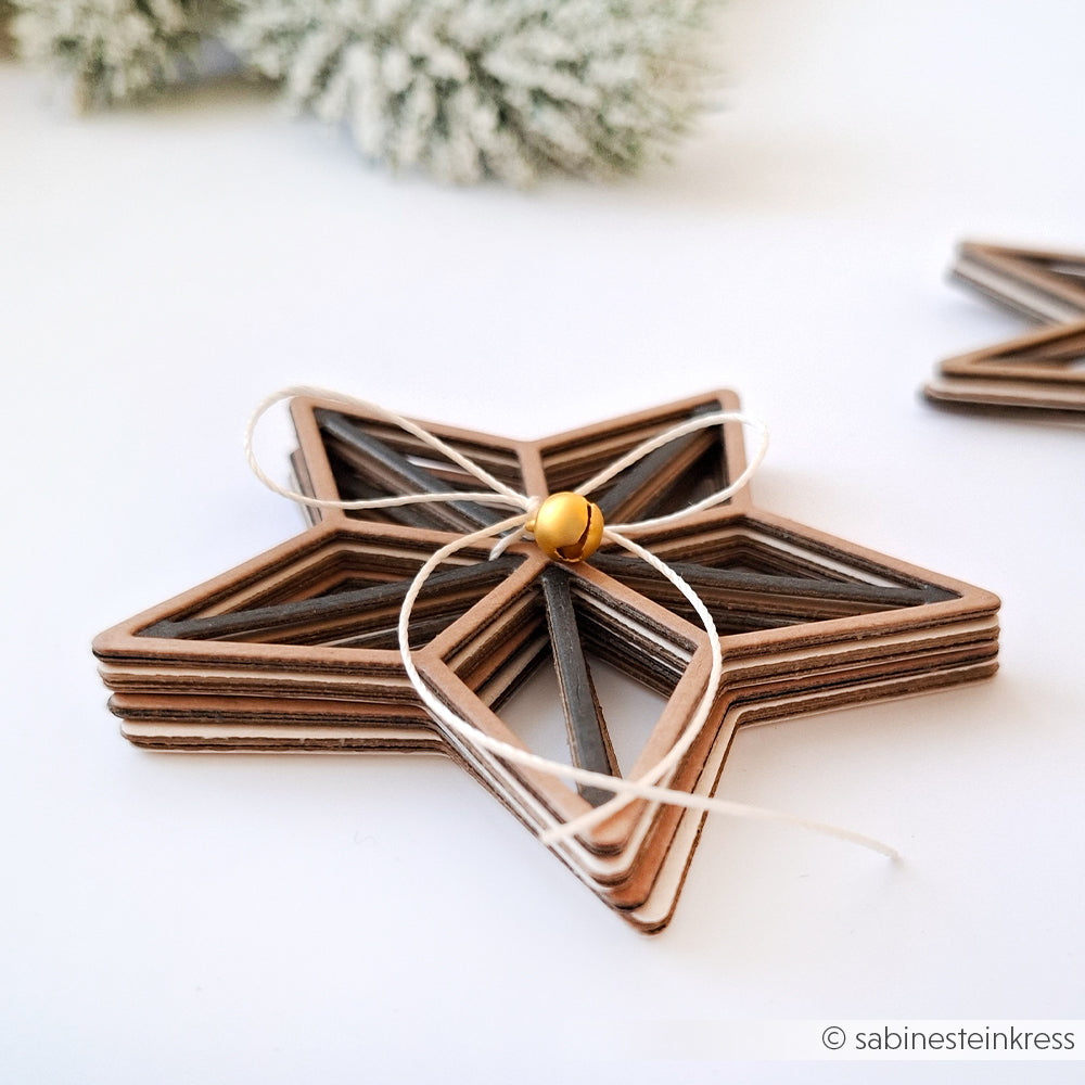 Ein Stapel Alexandra Renke Holzsterne, mit Schnur gebunden, und ein kleines Glöckchen, perfekt für Bastelkreationen, mit einem verschwommenen immergrünen Hintergrund.