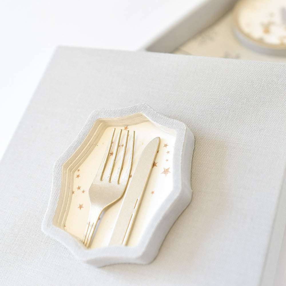 Eine silberne Gabel und ein silbernes Messer ruhen auf einem kleinen sechseckigen Teller mit Sternmuster, gefertigt mit der Motivstanze Vintageform von Alexandra Renke, auf einer strukturierten hellen Oberfläche.