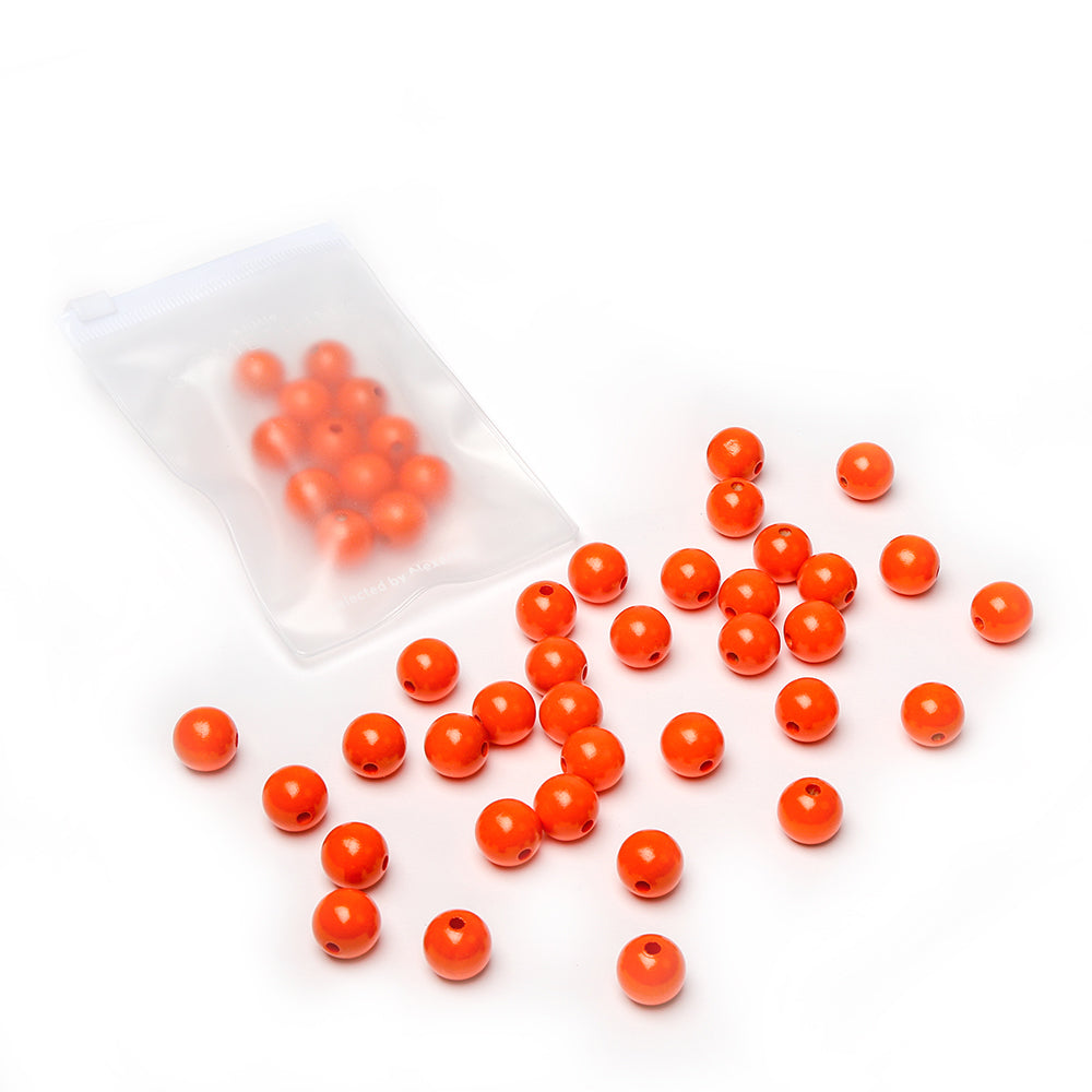 Leuchtend orangefarbene, runde Holzperlen von Alexandra Renke sind auf einer weißen Unterlage verstreut, wobei sich einige Perlen in einem durchsichtigen, wiederverschließbaren Plastikbeutel befinden – perfekt für Ihr nächstes Bastelprojekt mit nachhaltigem Holz.