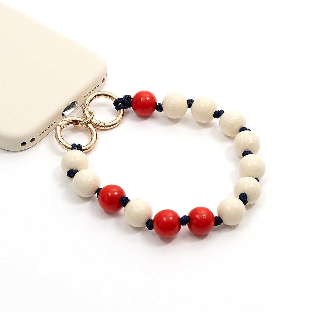 Rot-weißes Handyband mit Perlen von Alexandra Renke, mit Akzenten aus nachhaltigem Holz und goldenen Ringen, befestigt an einer beigen Handyhülle vor weißem Hintergrund. Perfekt als stilvolles Bastelprojekt oder umweltfreundliches Accessoire.