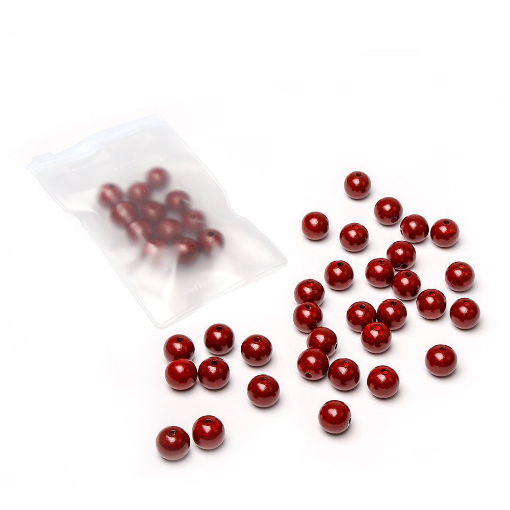 Alexandra Renkes rote, runde Holzperlen, verstreut auf einer weißen Unterlage, dazu weitere Perlen in einem durchsichtigen, wiederverschließbaren Plastikbeutel – perfekt für Ihr nächstes Bastelprojekt.
