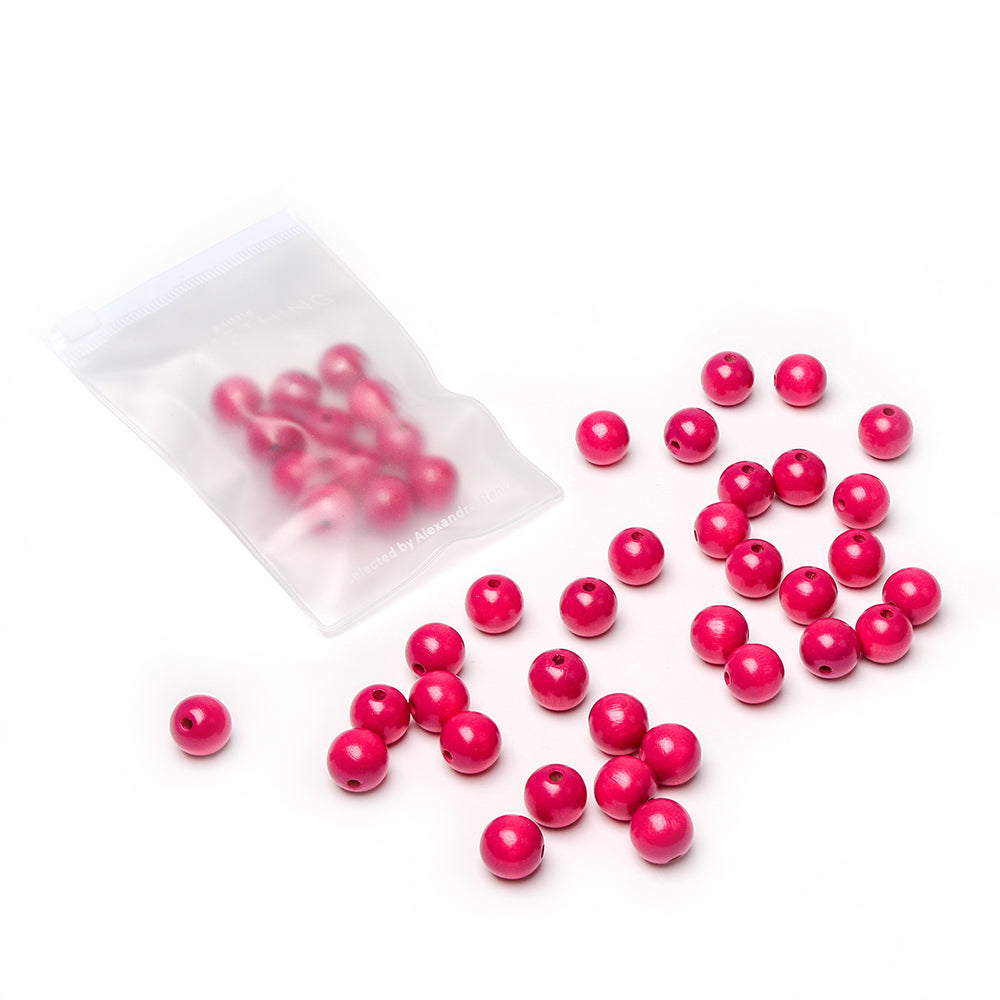 Alexandra Renke: Rote Perlen und Holzperlen sind auf einer weißen Fläche verstreut, einige davon befinden sich in einem kleinen durchsichtigen Plastikbeutel – perfekt für dein nächstes Bastelprojekt.