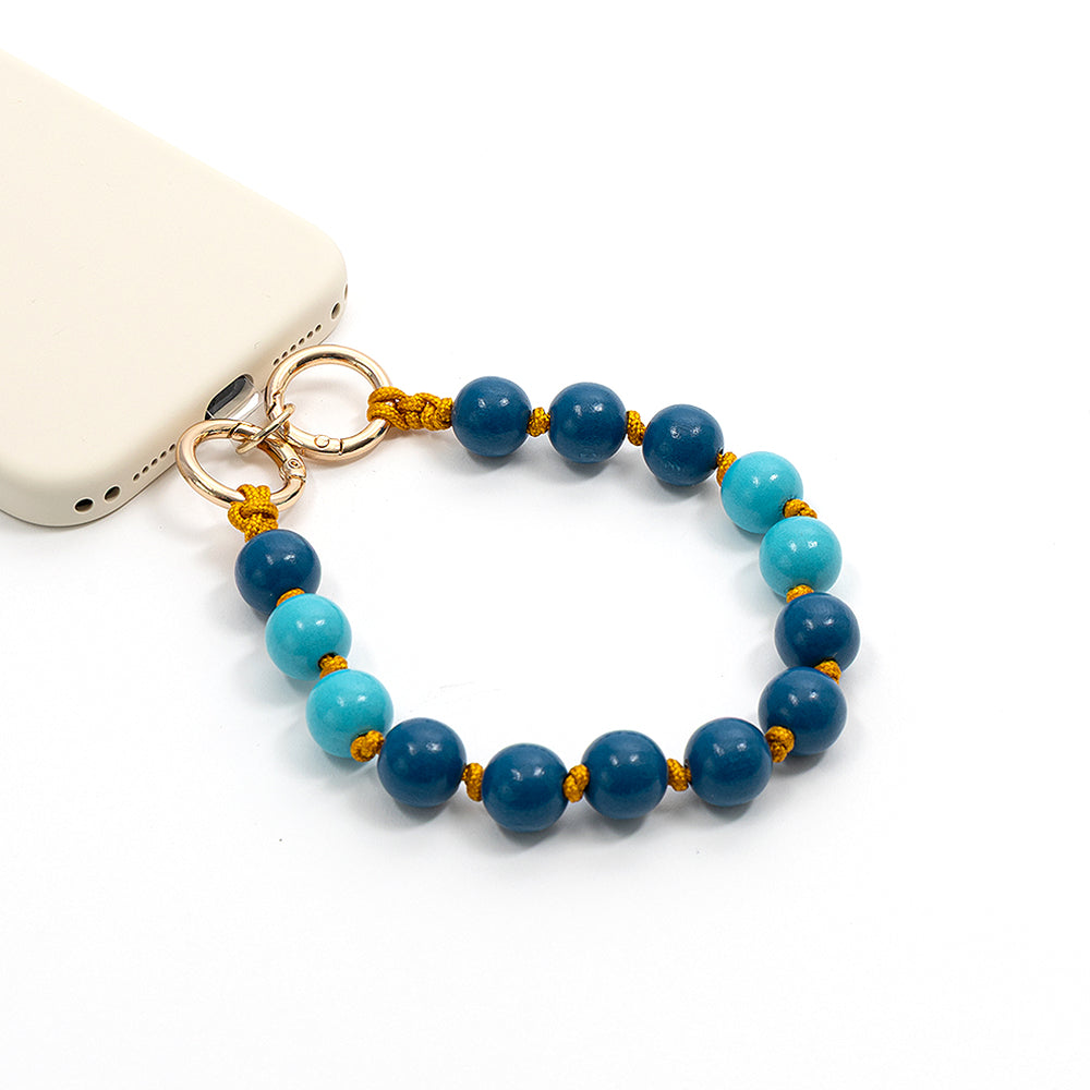 Ein mit Holzperlen verziertes Handyband mit abwechselnd dunkel- und hellblauen Holzperlen von Alexandra Renke, befestigt an einer weißen Handyhülle – perfekt als charmantes Bastelprojekt oder als umweltfreundliches Accessoire aus nachhaltigem Holz.
