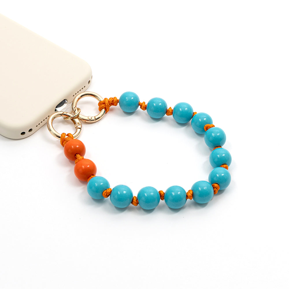 Perlen-Handyanhänger von Alexandra Renke mit blauen und orangefarbenen Perlen, darunter Holzperlen aus nachhaltigem Holz, befestigt an einer beigen Handyhülle vor weißem Hintergrund – perfekt für dein nächstes Bastelprojekt.