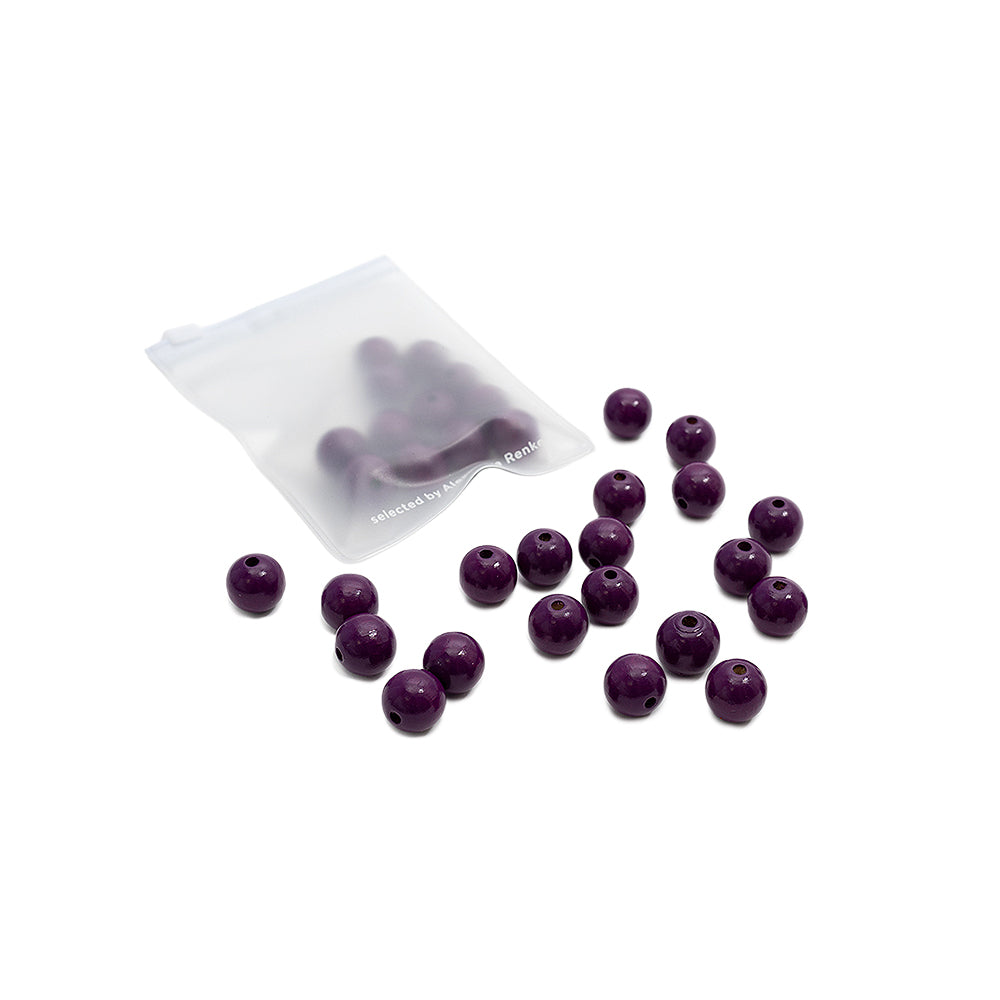 Kleine lila Holzperlen von Alexandra Renke, verstreut auf einer weißen Unterlage, wobei sich einige Perlen in einem durchsichtigen, wiederverschließbaren Plastikbeutel befinden – ideal für DIY-Schmuck und Bastelprojekte.