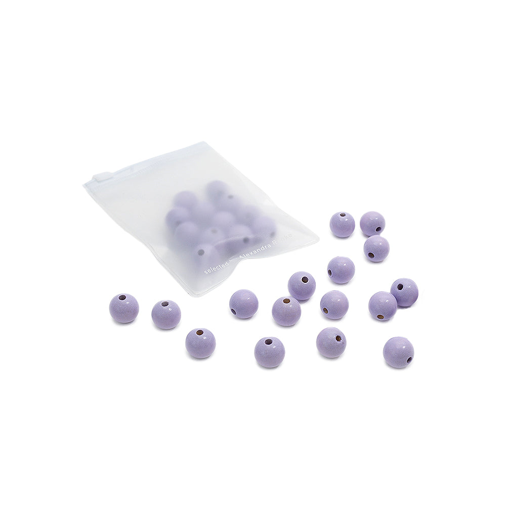 Ein kleines Säckchen mit violetten, runden Holzperlen von Alexandra Renke mit Löchern, ideal für DIY-Schmuckprojekte, wobei einige Perlen außerhalb des Säckchens auf weißem Hintergrund verstreut sind.