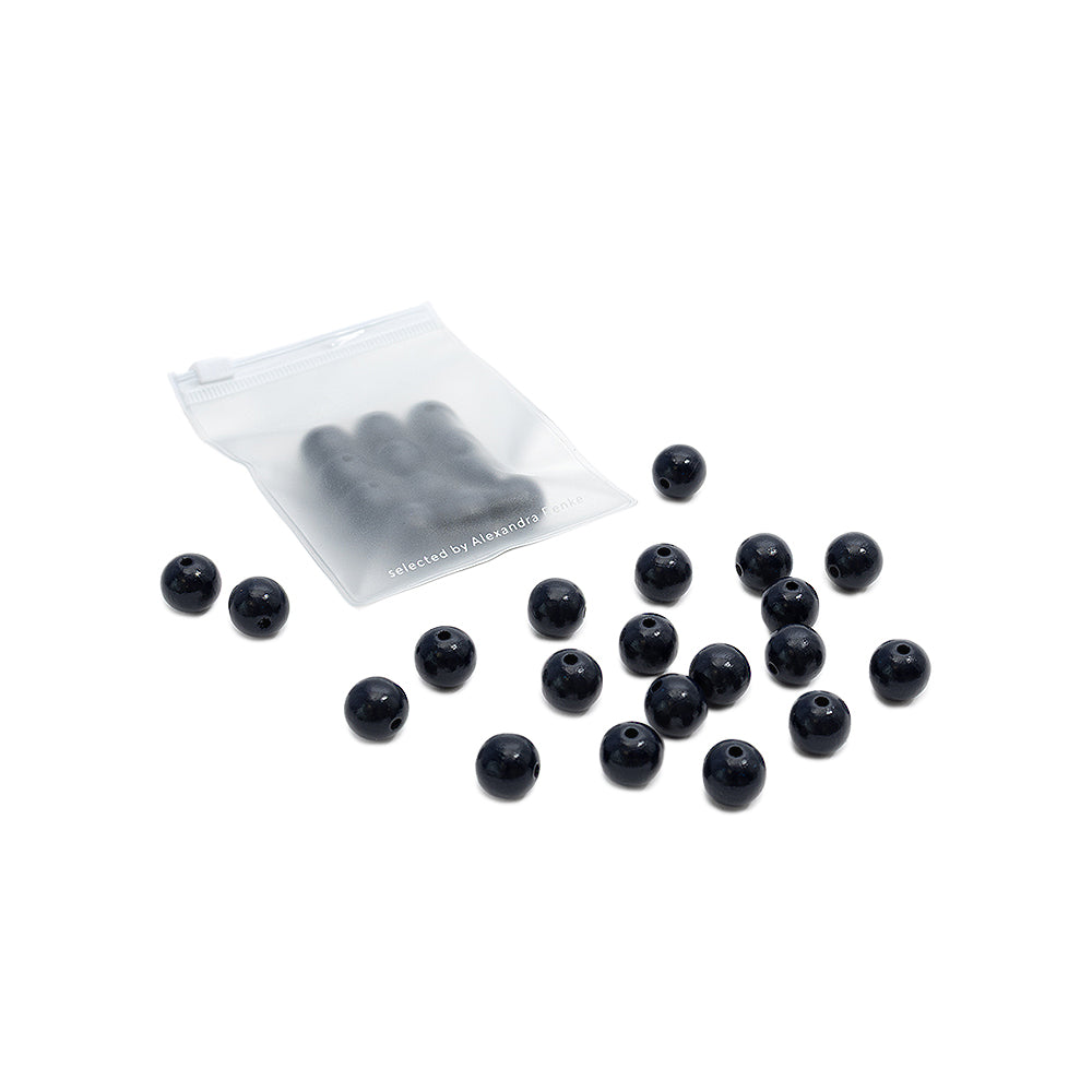 Kleine schwarze Holzperlen von Alexandra Renke, verstreut neben einem durchsichtigen, wiederverschließbaren Beutel, in dem sich weitere Perlen befinden, vor einem weißen Hintergrund – perfekt für jedes Bastelprojekt mit nachhaltigem Holz.
