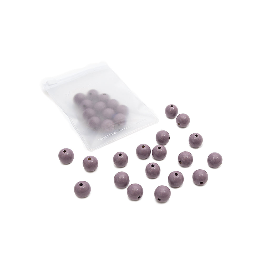 Ein kleines Säckchen von Alexandra Renke mit violetten runden Perlen, von denen sich einige im Säckchen befinden und andere außen verstreut sind – perfekt für dein nächstes Bastelprojekt und mit wunderschönen Holzperlen aus nachhaltigem Holz.
