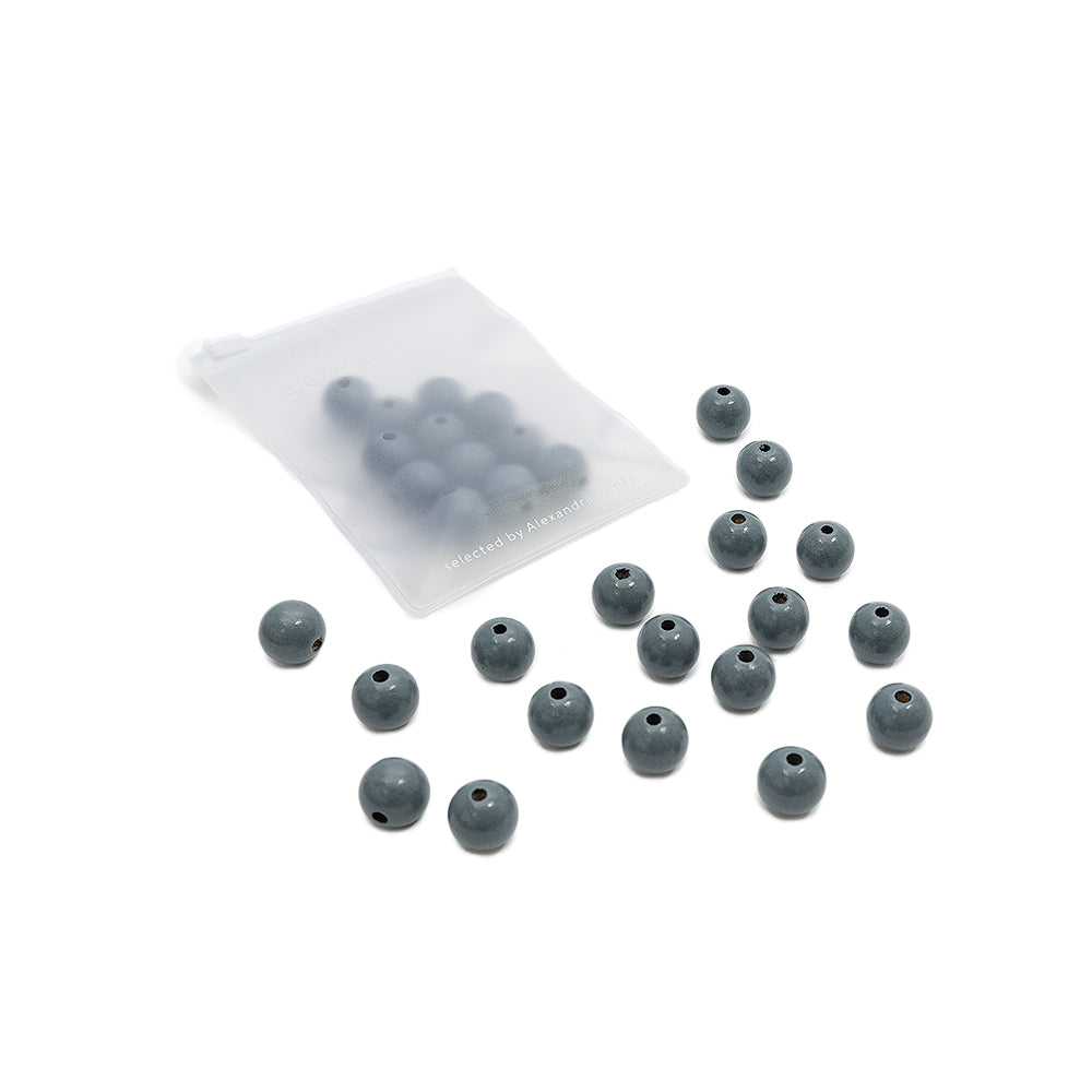 Siebzehn runde, graue Holzperlen von Alexandra Renke liegen verstreut da, und im Hintergrund befinden sich weitere Perlen in einem mattierten Plastikbeutel – perfekt für jedes Bastelprojekt oder jede kreative Arbeit aus nachhaltigem Holz.
