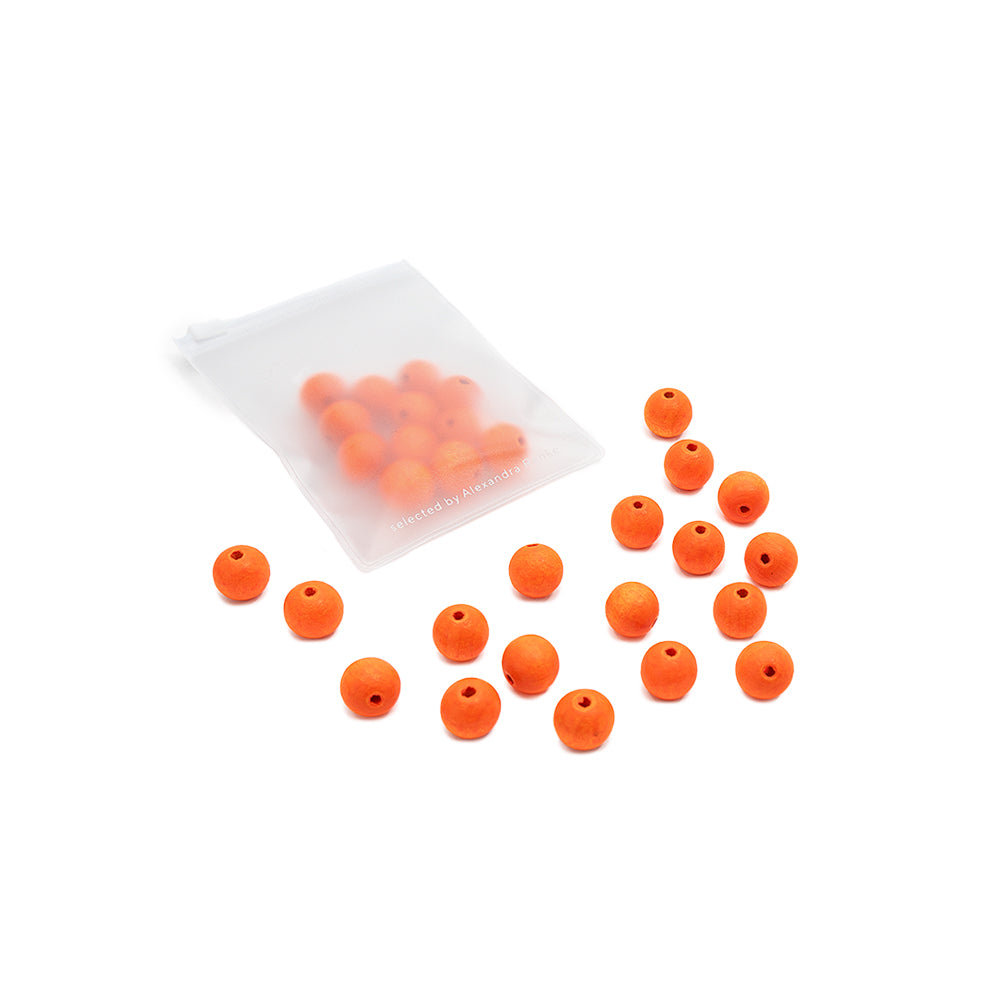 Ein mattes Säckchen mit orangefarbenen Holzperlen von Alexandra Renke, von denen sich einige im Inneren befinden und andere auf einer weißen Fläche verstreut sind – perfekt als Inspiration für dein nächstes Bastelprojekt oder um selbst Schmuck herzustellen.