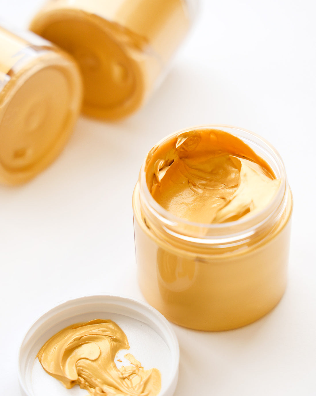 Offene Dose mit goldgelber Creme oder Farbe ohne Deckel, umgeben von ähnlichen geschlossenen Dosen.