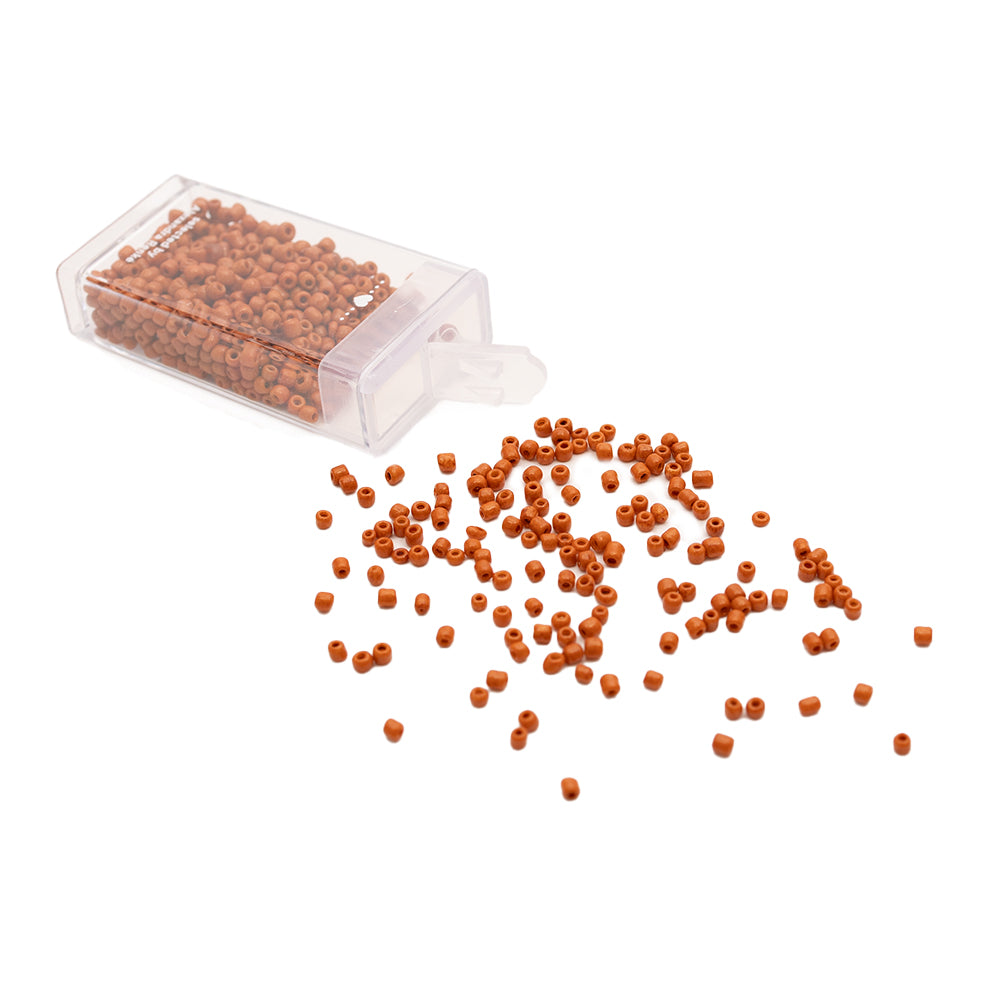 Kleine orangefarbene Glasperlen von Alexandra Renke rieseln aus einem durchsichtigen Plastikbehälter auf eine weiße Fläche und verleihen ihr den Charme einer Vintage-Optik.