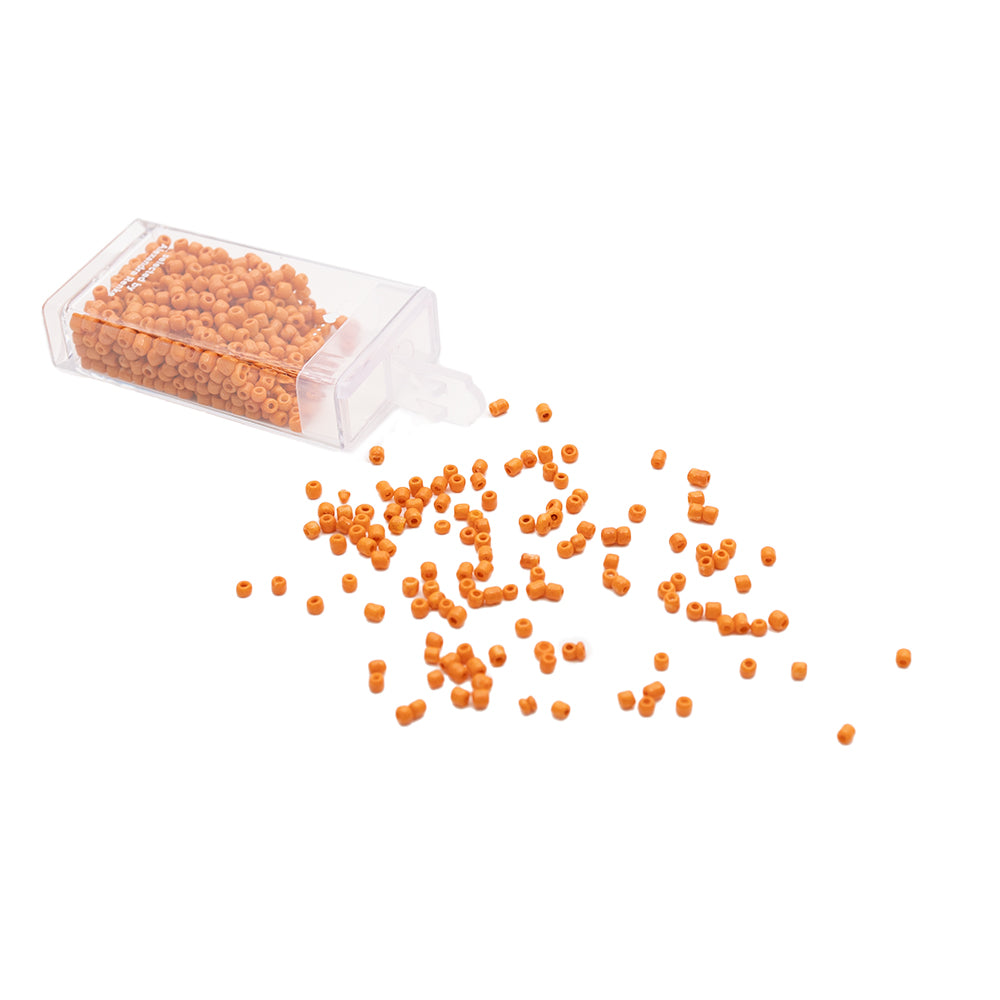 Kleine orangefarbene Rocailles-Perlen von Alexandra Renke rieseln aus einem durchsichtigen Plastikbehälter auf eine weiße Fläche und sorgen so für einen bezaubernden Vintage-Look.